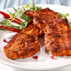 Dwa soczyste kawałki boczku na grilla, przyprawione i udekorowane papryczkami chili i zieleniną.