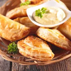 Złociste pierogi meksykańskie, pieczone i podane z sosem dip i natką pietruszki w wiklinowym koszyku.
