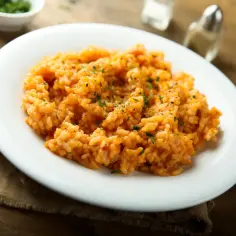 Kremowe risotto pomidorowe, idealne do przygotowania którego potrzebny jest specjalny ryż. Posypane natką pietruszki i pieprzem.