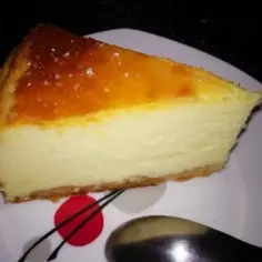 Pyszny sernik z jogurtu greckiego z lekko skarmelizowaną górą, podany na białym talerzu.