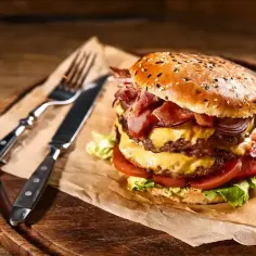 Podwójny burger z bekonem i serem, idealny na prawdziwe burgery przepis. Obok nóż i widelec.