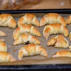 Szybkie rogaliki kruche, świeżo upieczone, leżą na blasze wyłożonej papierem do pieczenia.