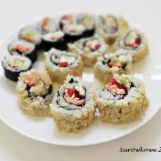Różne rodzaje sushi na talerzu: maki z łososiem, awokado i ogórkiem, niektóre obtoczone w sezamie.