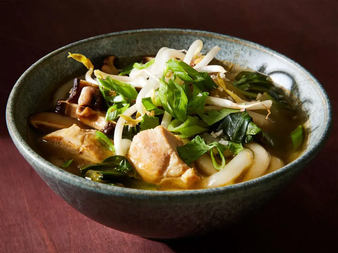 Miseczka z aromatycznym udon przepisem: gruby makaron, kawałki kurczaka, grzyby shiitake, kiełki fasoli mung i zielona cebulka w bulionie.