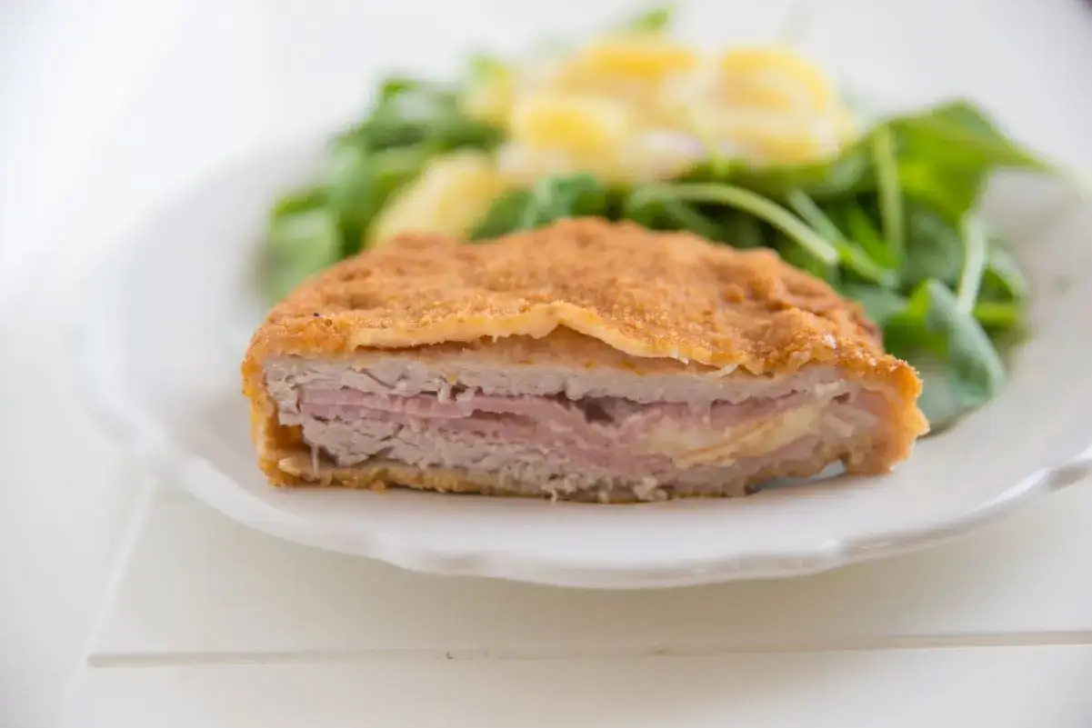 Kotlet po szwajcarsku, panierowany, z soczystym mięsem, szynką i rozpływającym się serem. Podany z sałatką.