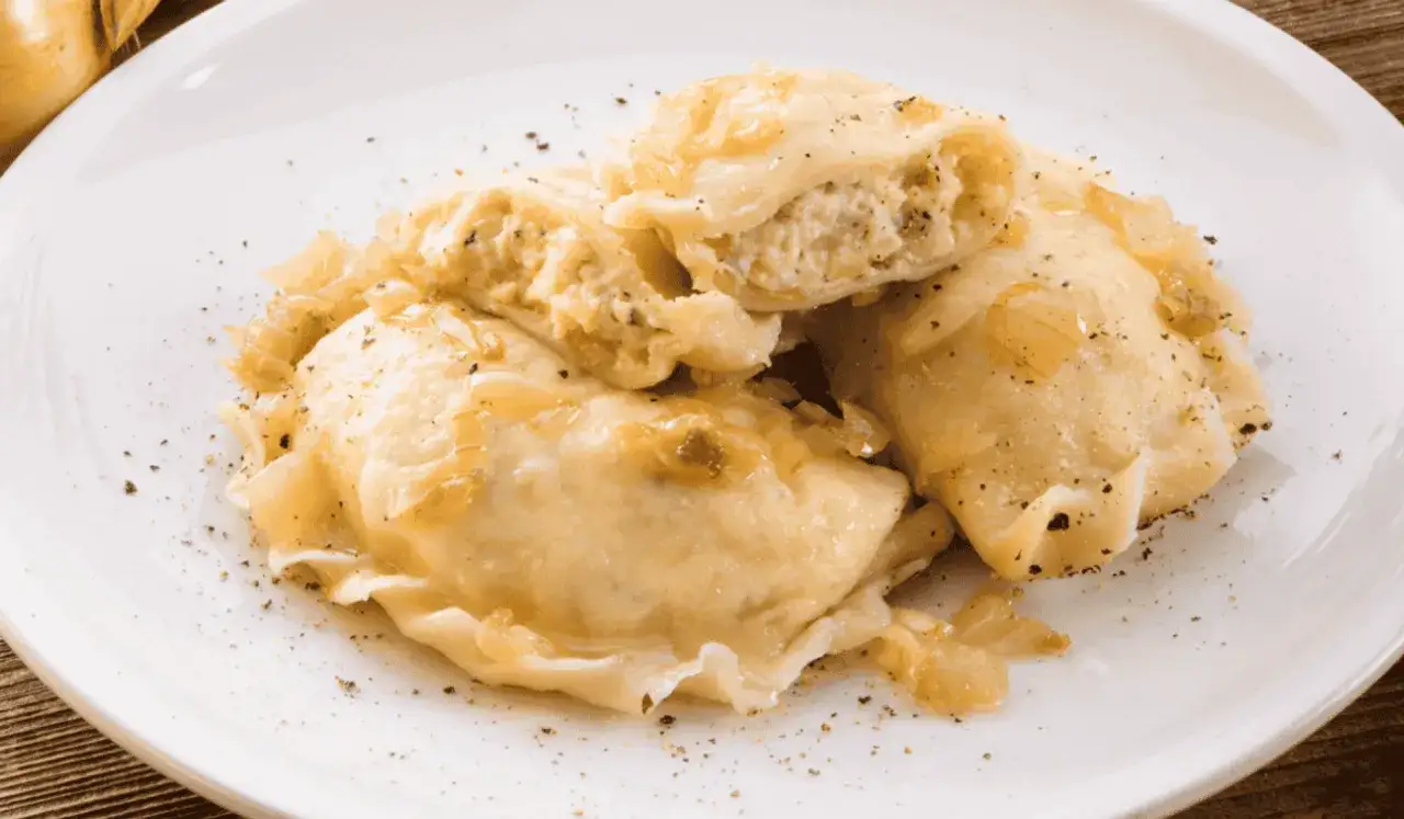 Pierogi ruskie z serem i ziemniakami, polane skarmelizowaną cebulką i posypane pieprzem. Pyszne i sycące danie.