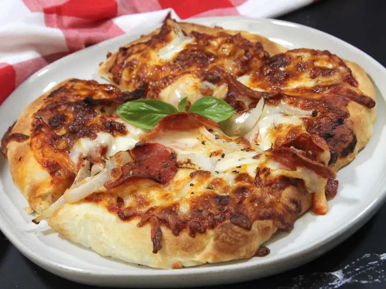 Pyszna pizza z air fryera z ciągnącym serem, pepperoni i cebulą, ozdobiona listkiem bazylii.