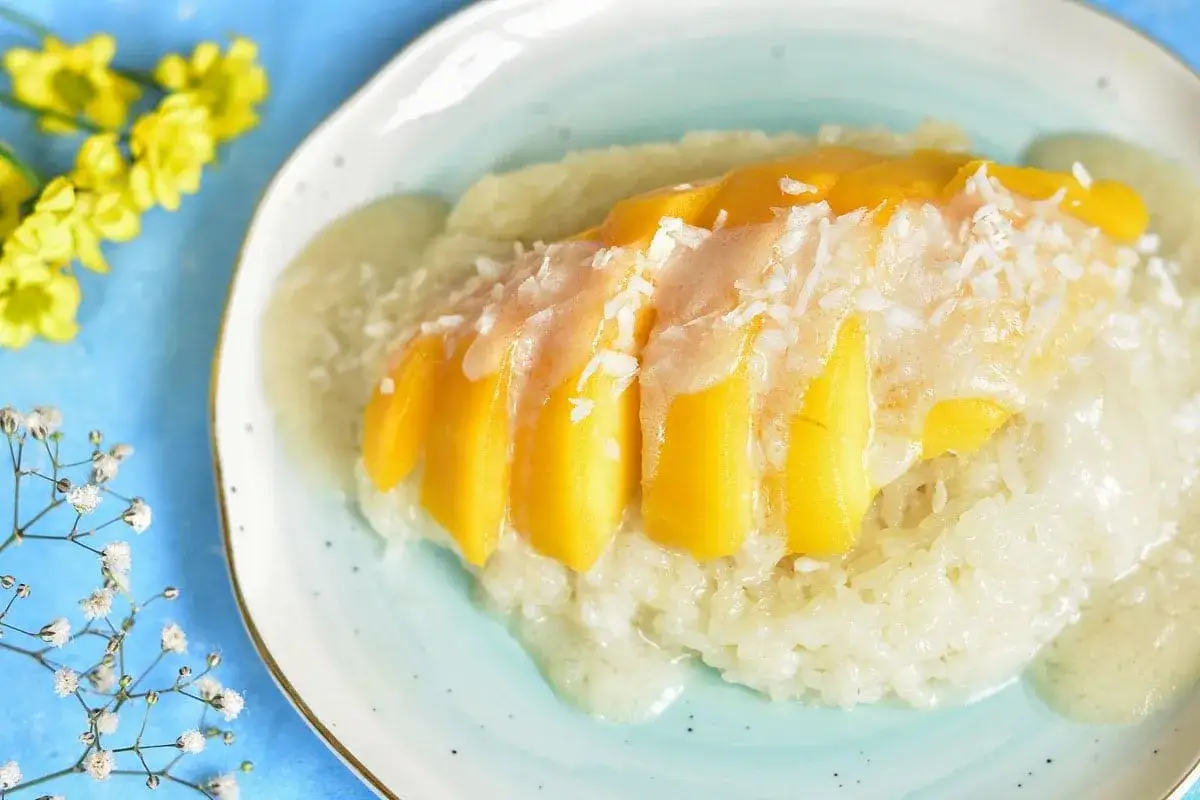 Pyszny deser mango sticky rice przepis: ryż zaparzony w mleku kokosowym, polany słodkim sosem, z kawałkami mango i wiórkami kokosowymi.