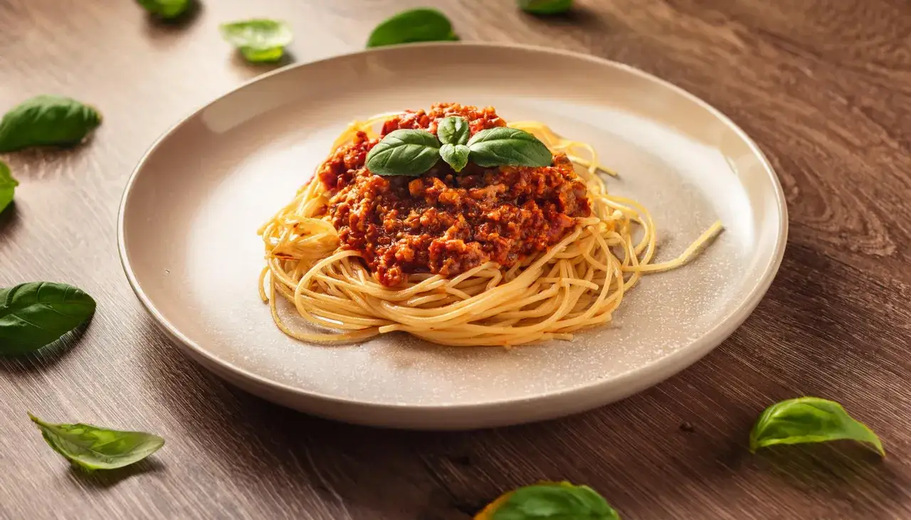 Pyszne spaghetti bolognese z bazylią na talerzu. Idealny przepis, jak zrobić spaghetti, by zachwycić bliskich.